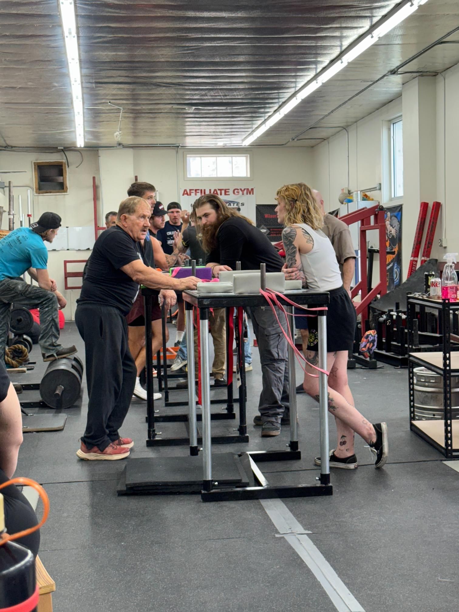 Arm wrestling competition in a gym. Competitors at tables, people watching.