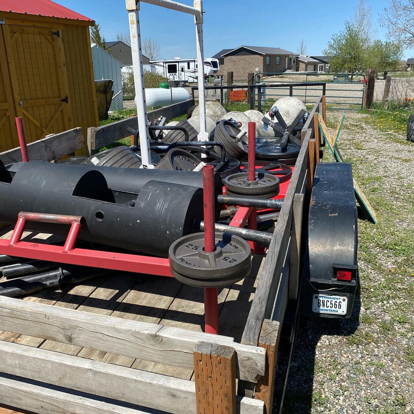 A trailer loaded with exercise equipment, including weight plates and a large black smoker.