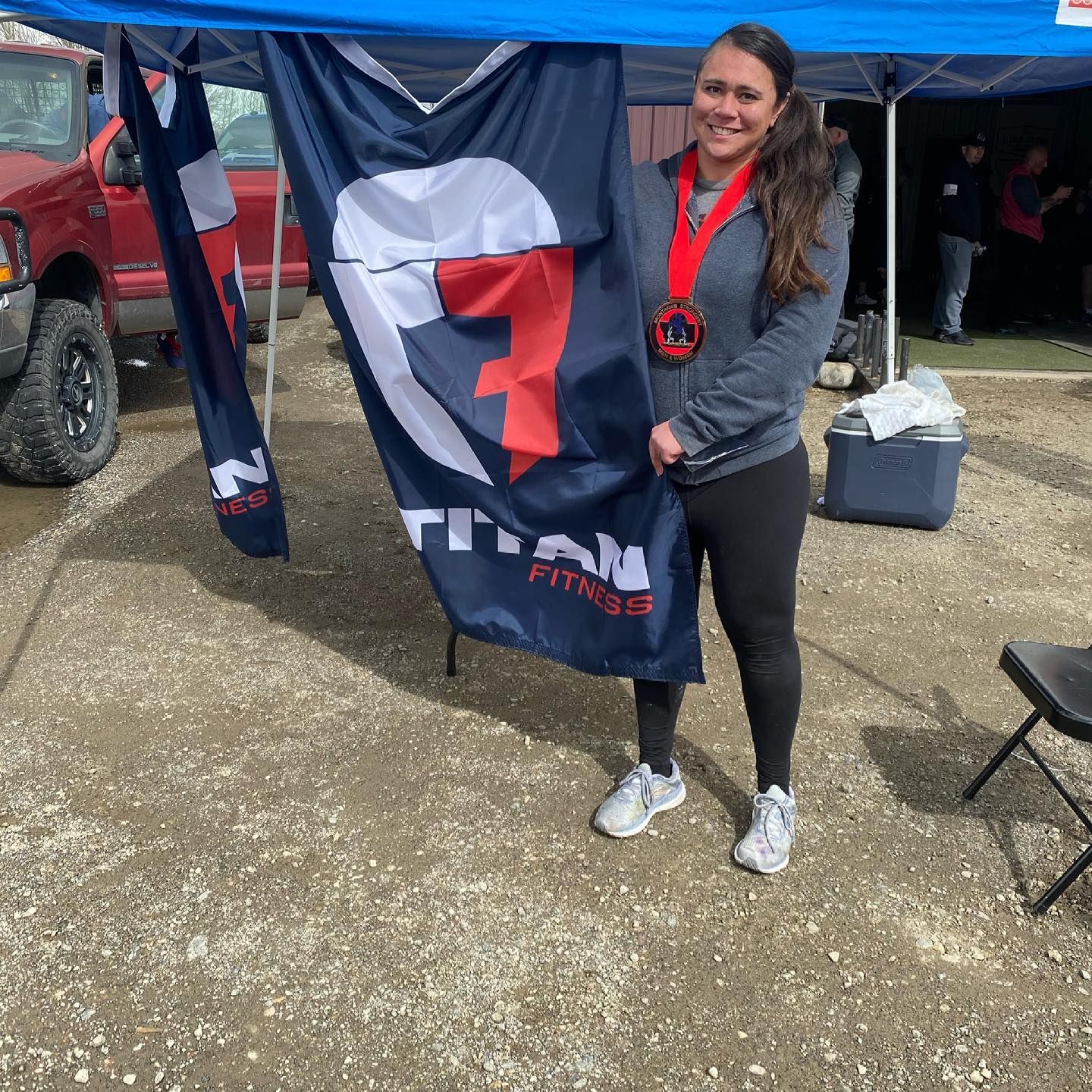 Woman holding a flag and medal, standing near a truck under a canopy.