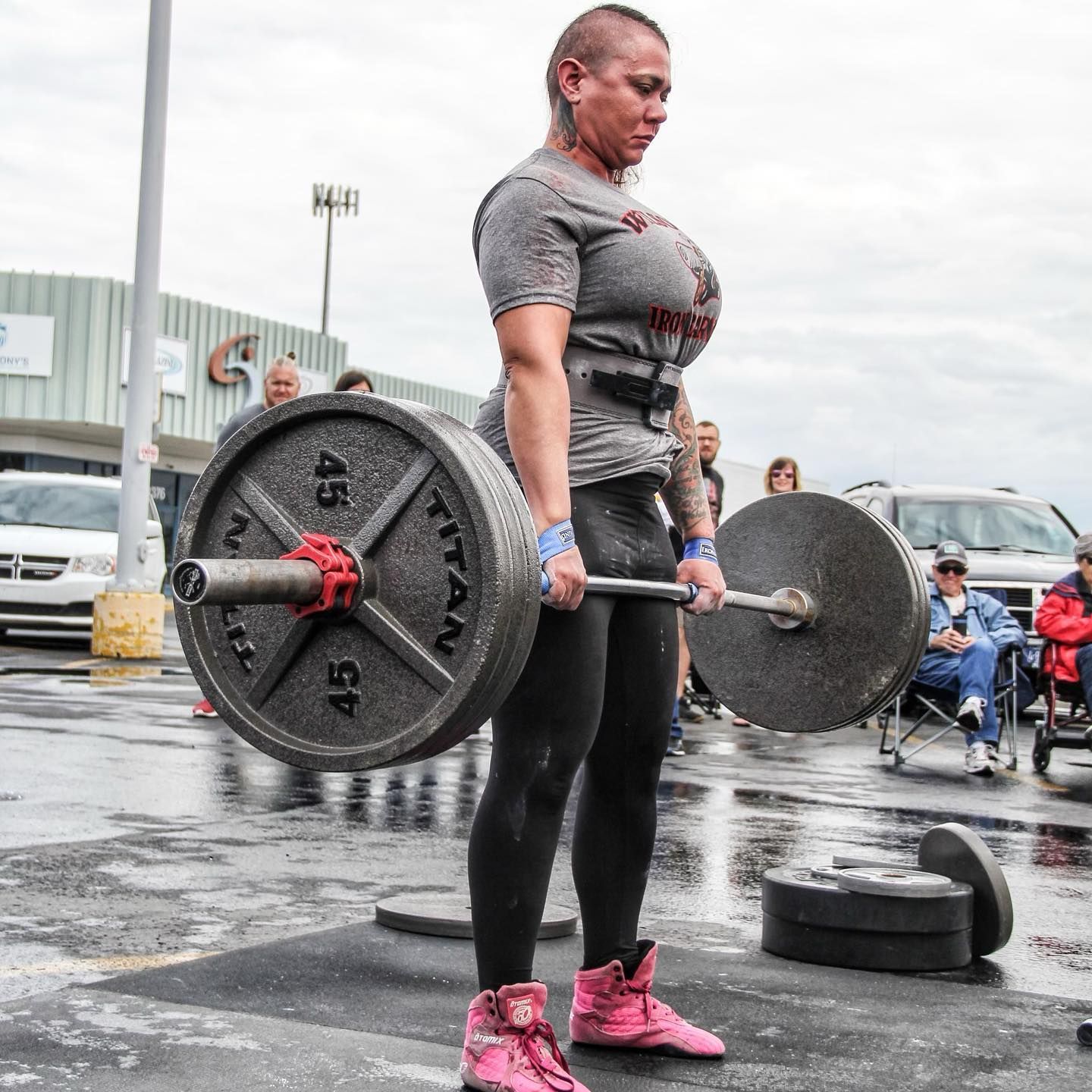 Woman in pink shoes deadlifting a barbell with weights on an outdoor platform.