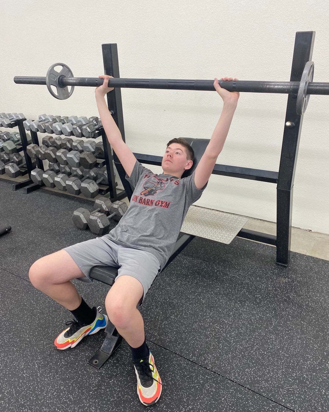Person lifting weights on a bench press in a gym. Arms extended upward, bar overhead.