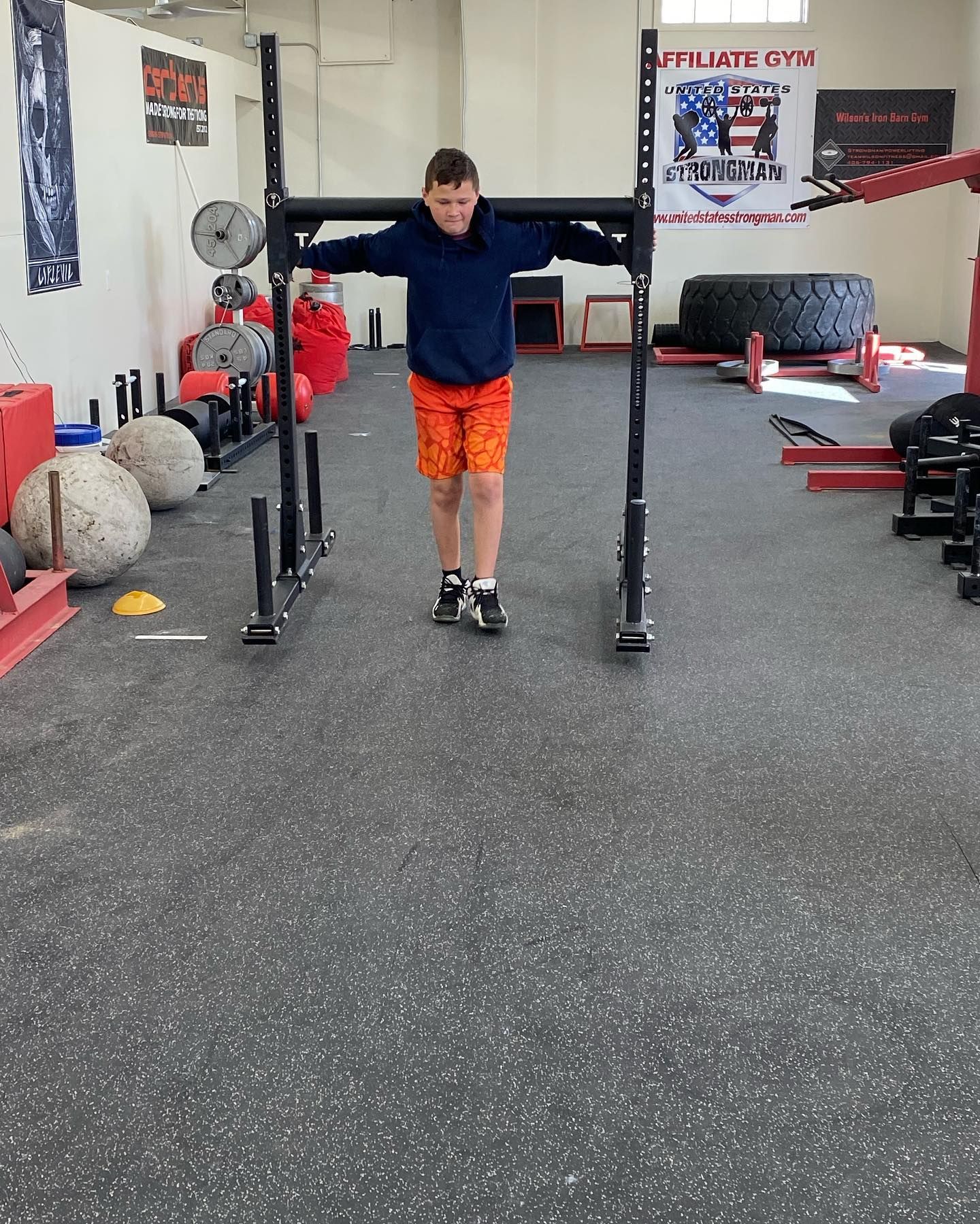 Person wearing a blue shirt and orange shorts pushing a metal sled in a gym.