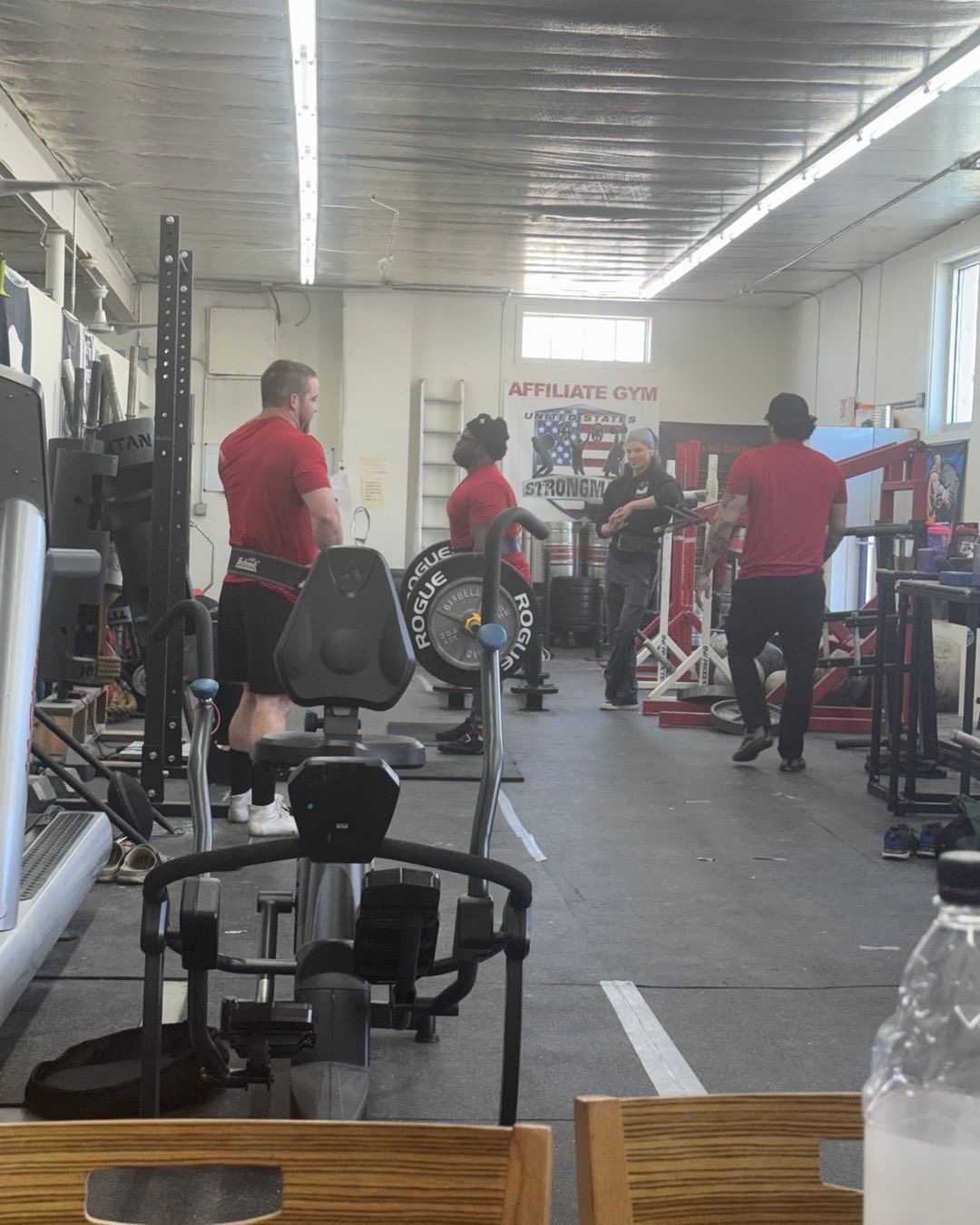 People lifting weights in a gym; some wearing red shirts.