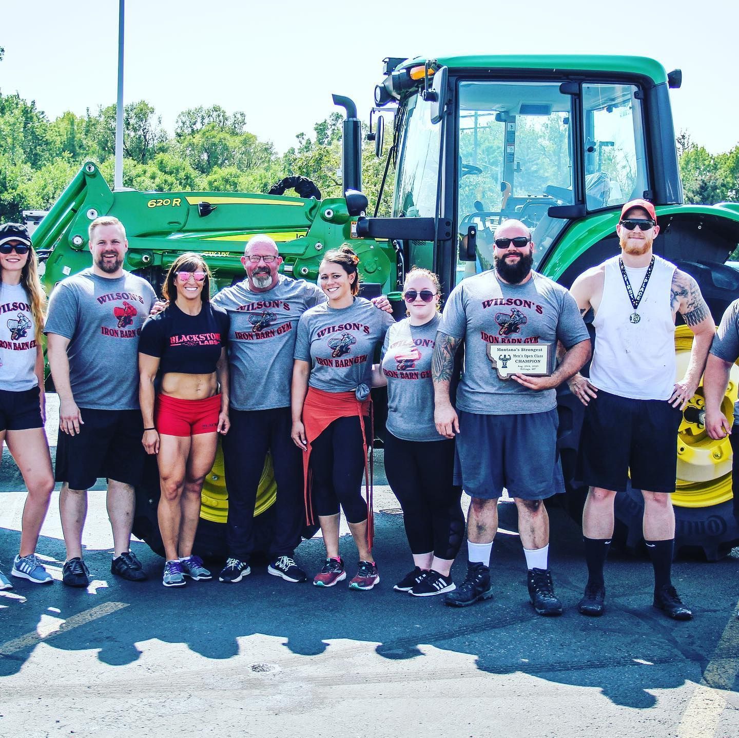 Group of people posing in front of a green tractor, likely at an outdoor event.