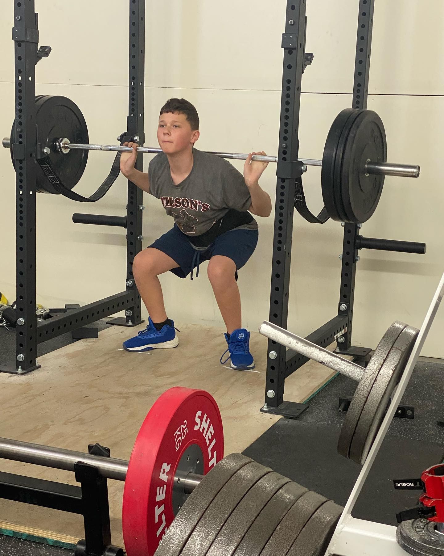 Young person squatting with a barbell in a gym. Wearing a weightlifting belt and lifting shoes.
