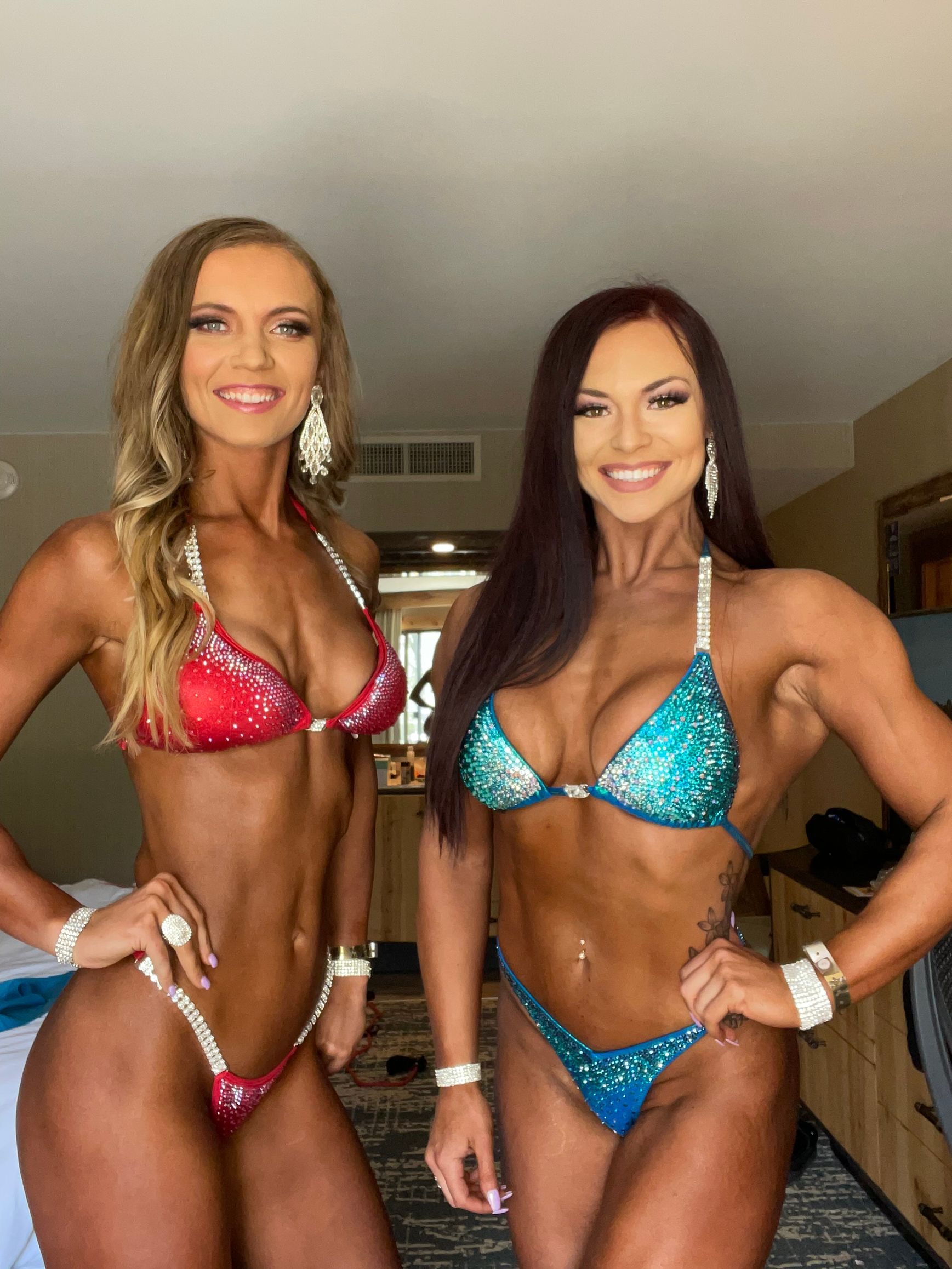 Two women in bikinis pose, tanned, with jewelry, arms on hips.
