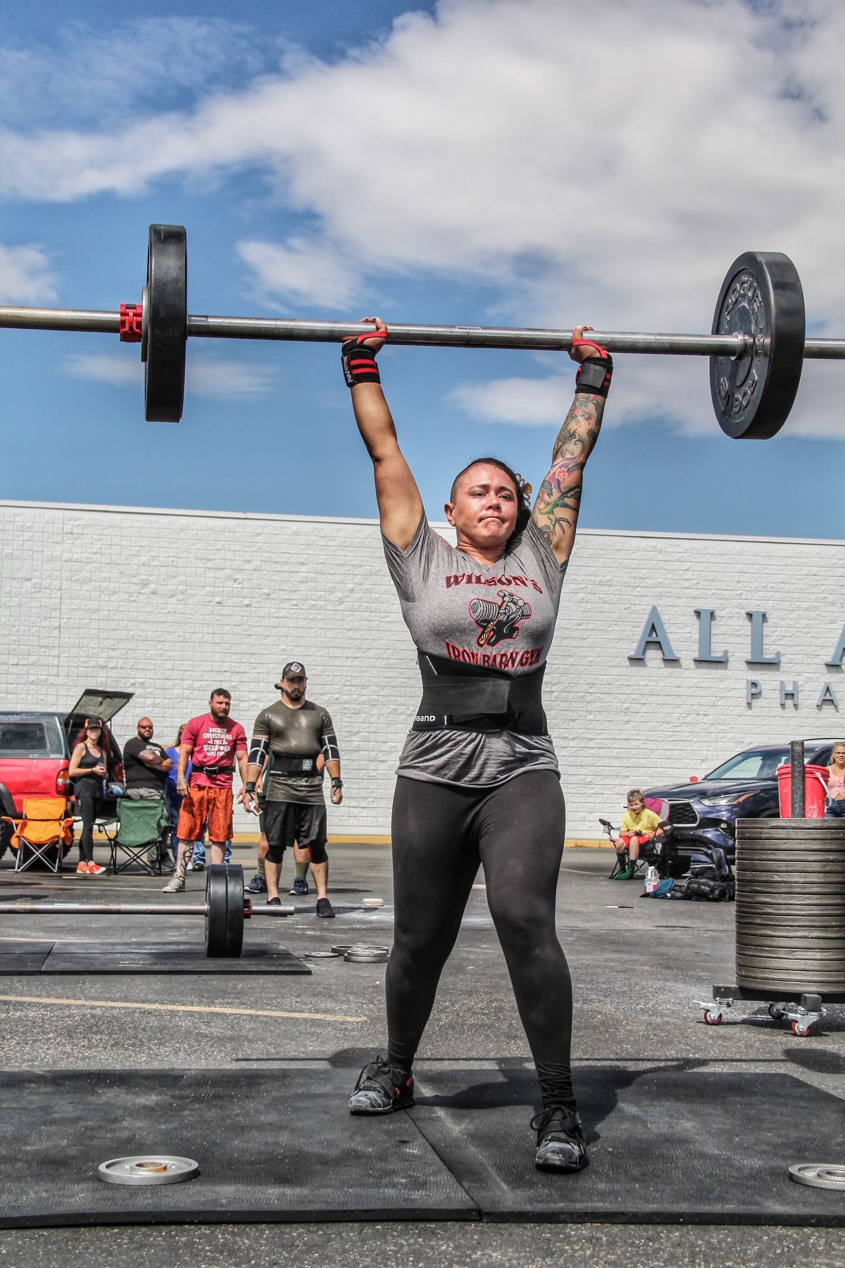 Woman lifting barbell overhead in outdoor competition.