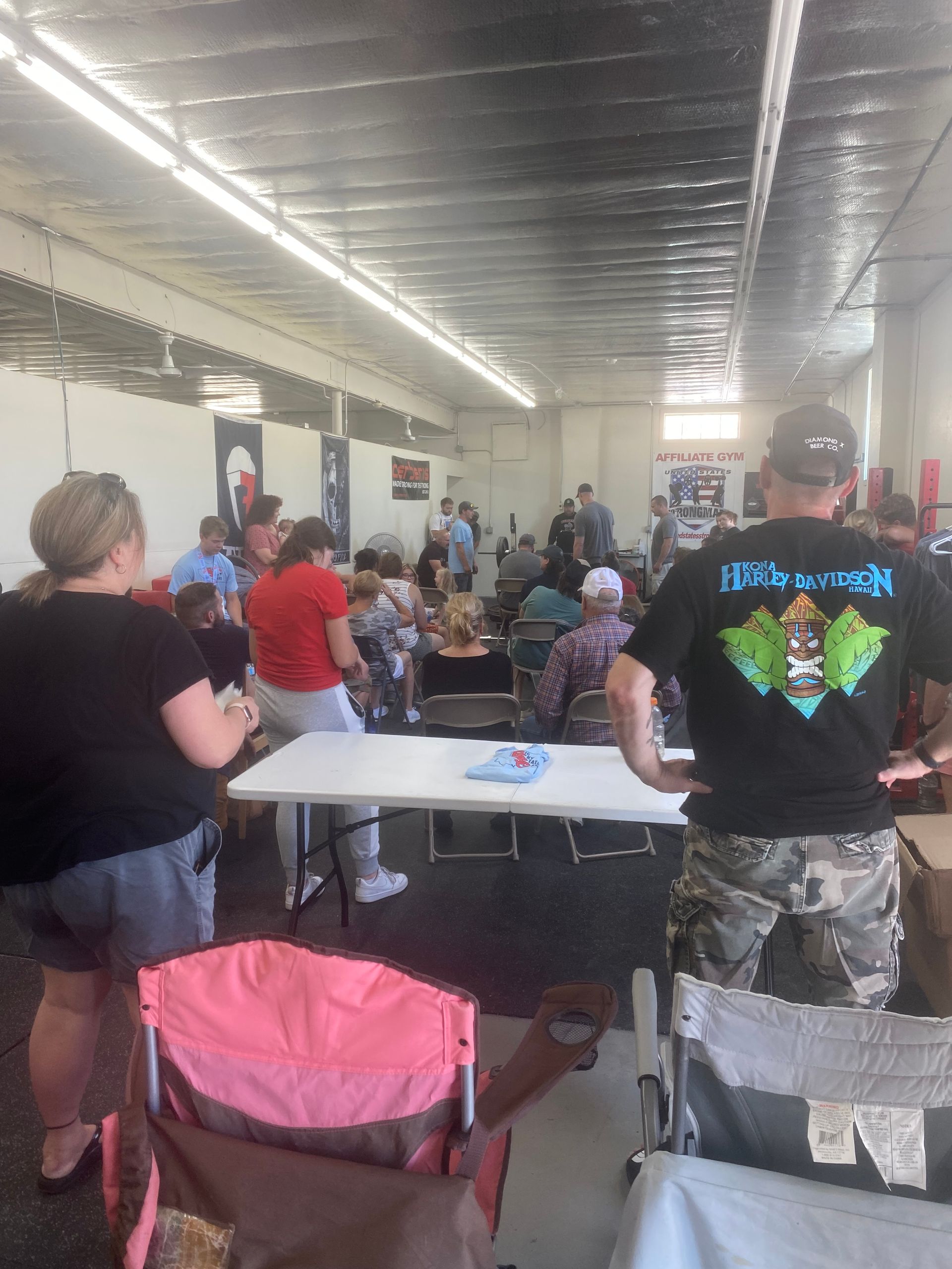 People gathered indoors, standing and sitting at tables. Several are looking towards a central area.