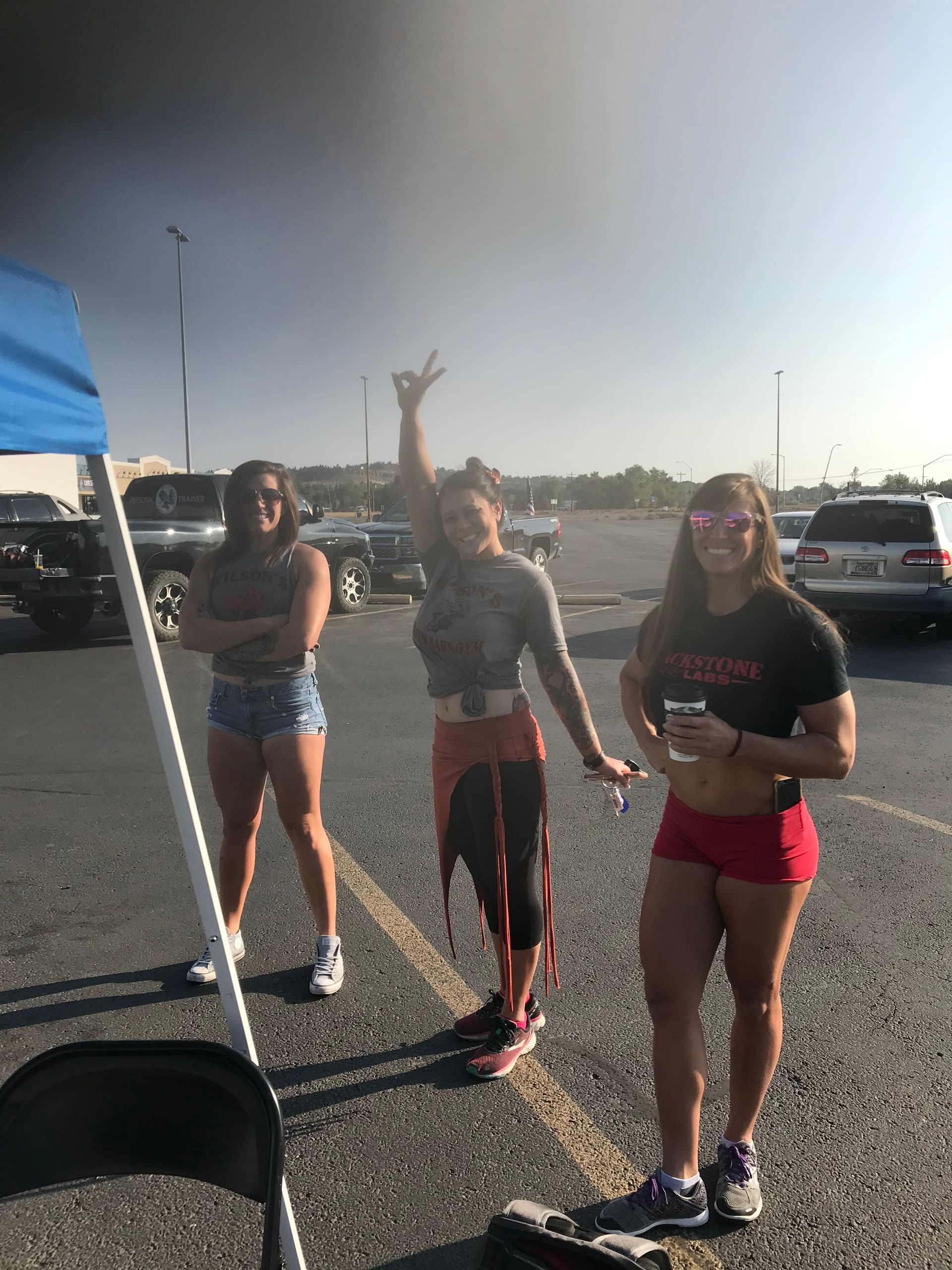 Three people standing in a parking lot. One raises a hand with a peace sign, others pose.