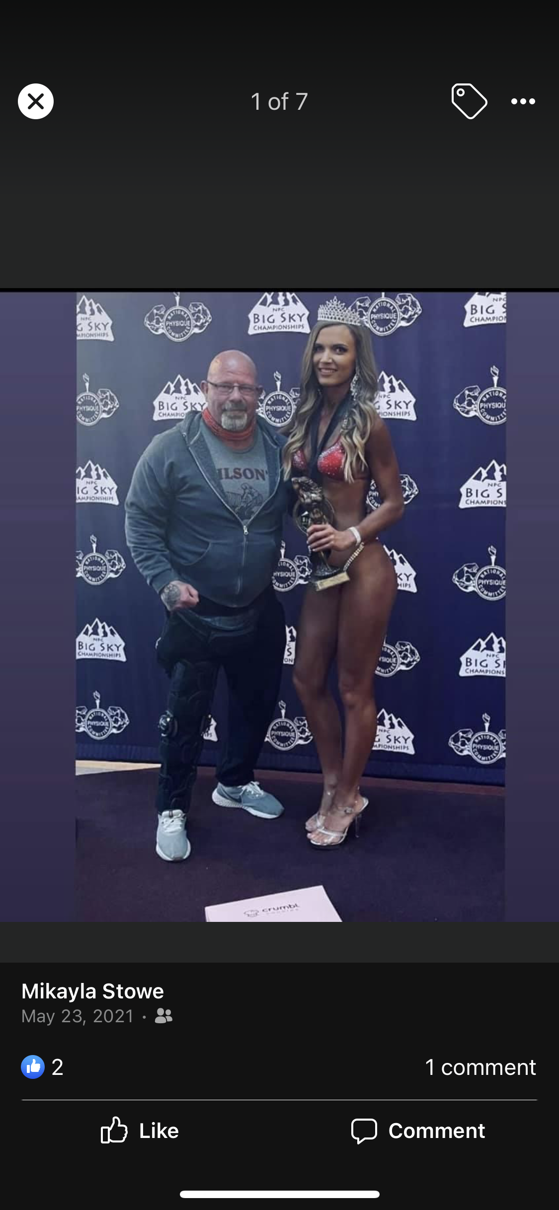 Man and woman in front of a banner. Woman in a bikini holds a trophy.