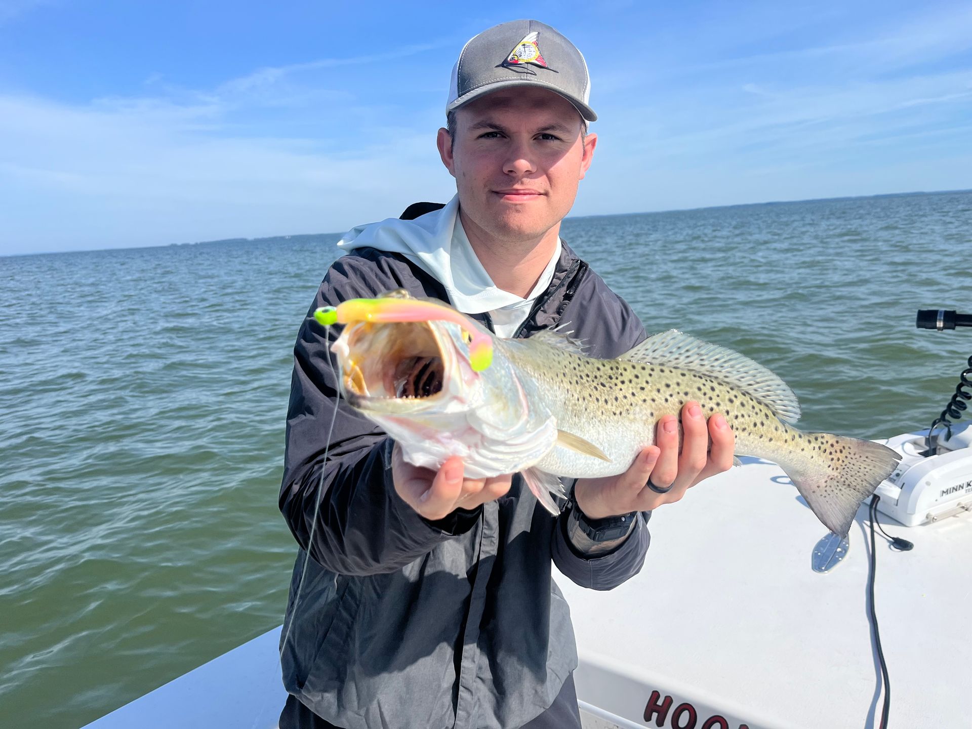 Man holding large striped bass on a boat at sunset.
