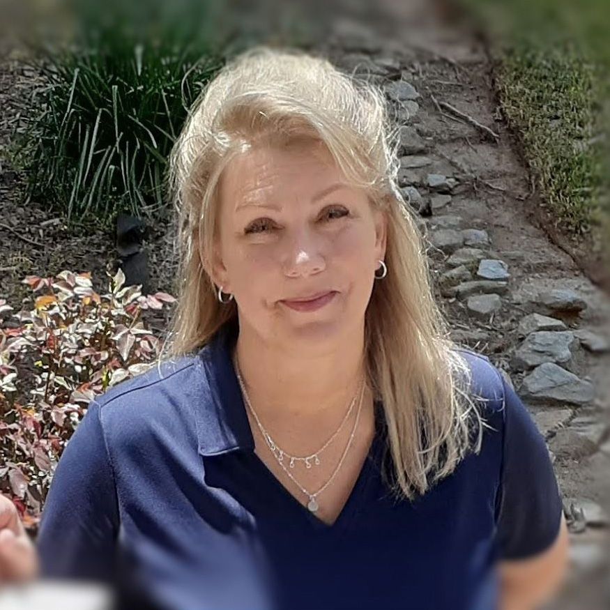 A woman wearing a blue shirt and a necklace is smiling for the camera.