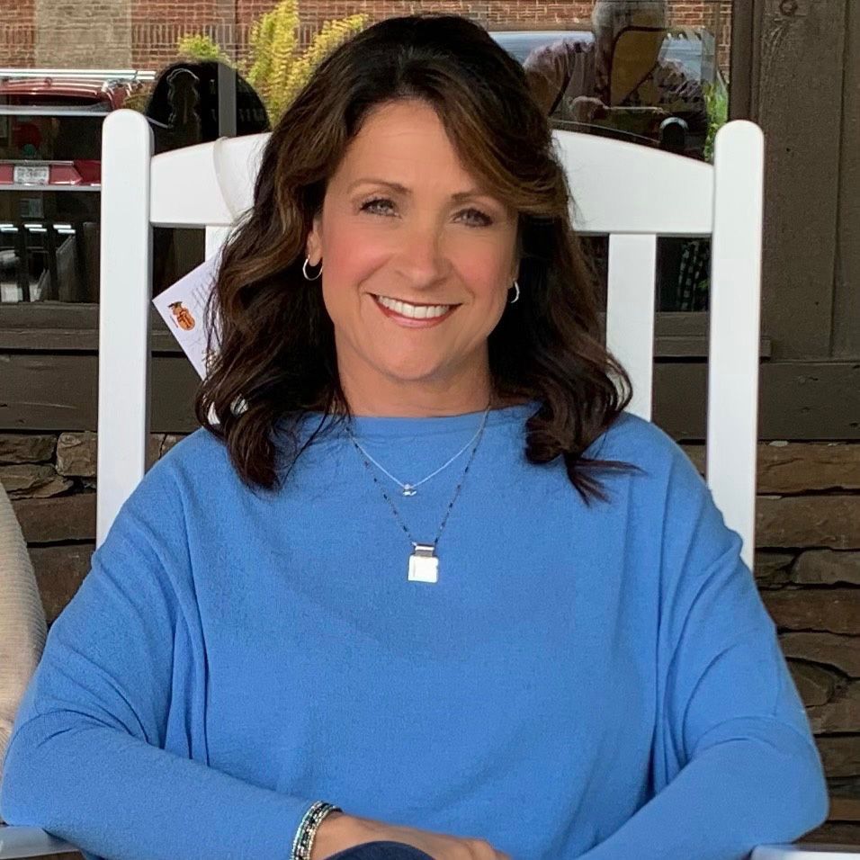 A woman in a blue sweater is sitting in a white chair and smiling.