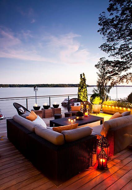 A wooden deck with a couch and lanterns overlooking a body of water