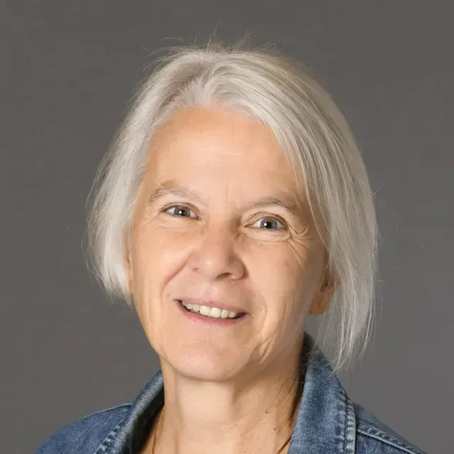 Eine Frau mit weissem Haar trägt eine Jeansjacke und lächelt.