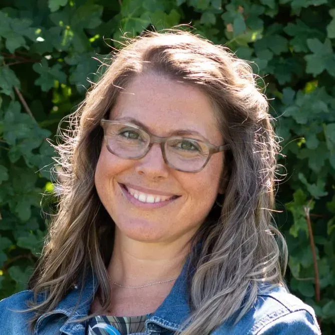 Eine Frau mit Brille und Jeansjacke lächelt in die Kamera.