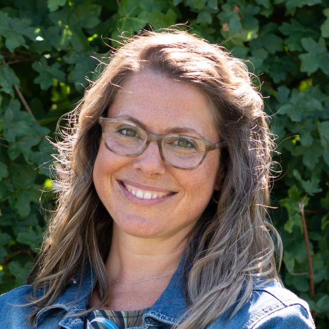 Eine Frau mit Brille und Jeansjacke lächelt in die Kamera.