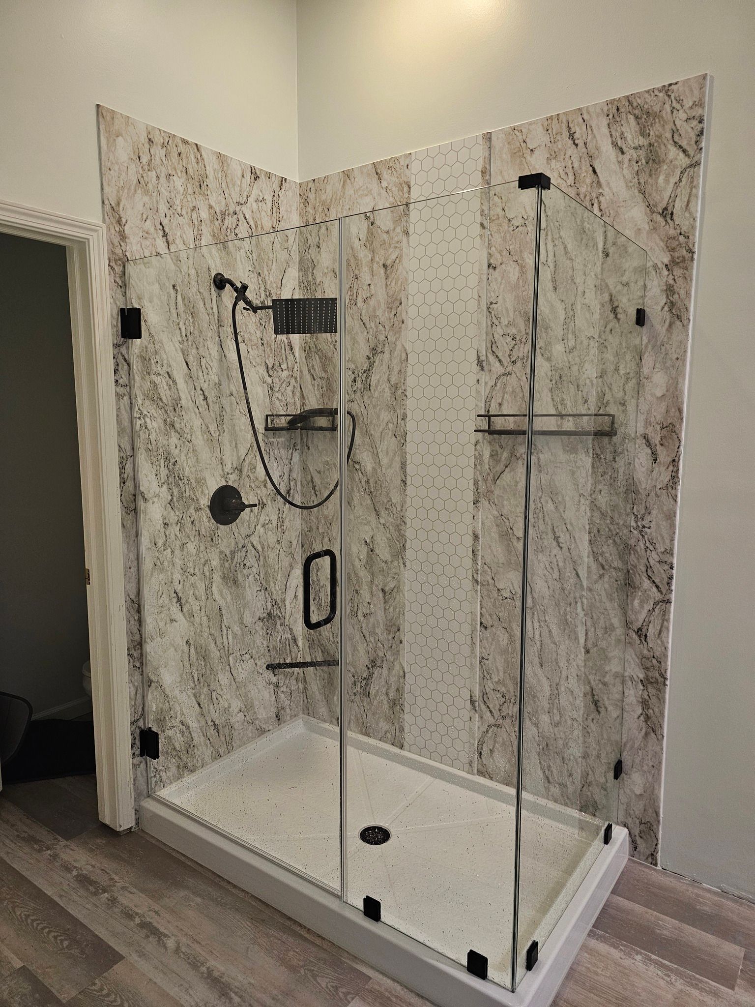 Corner shower with glass doors, black fixtures, and marble-look walls and floor.
