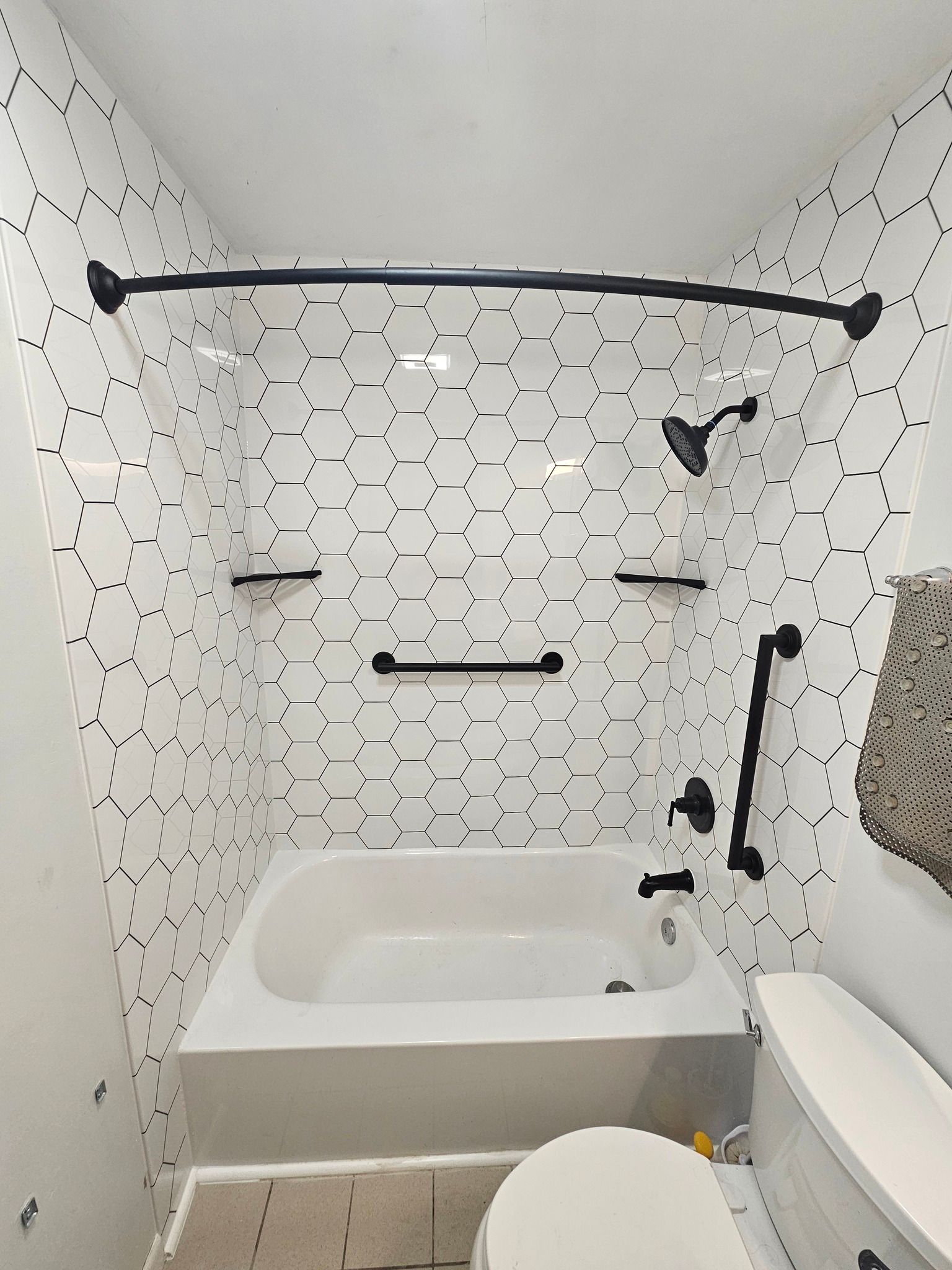 White tiled bathroom with black fixtures, tub, and toilet.