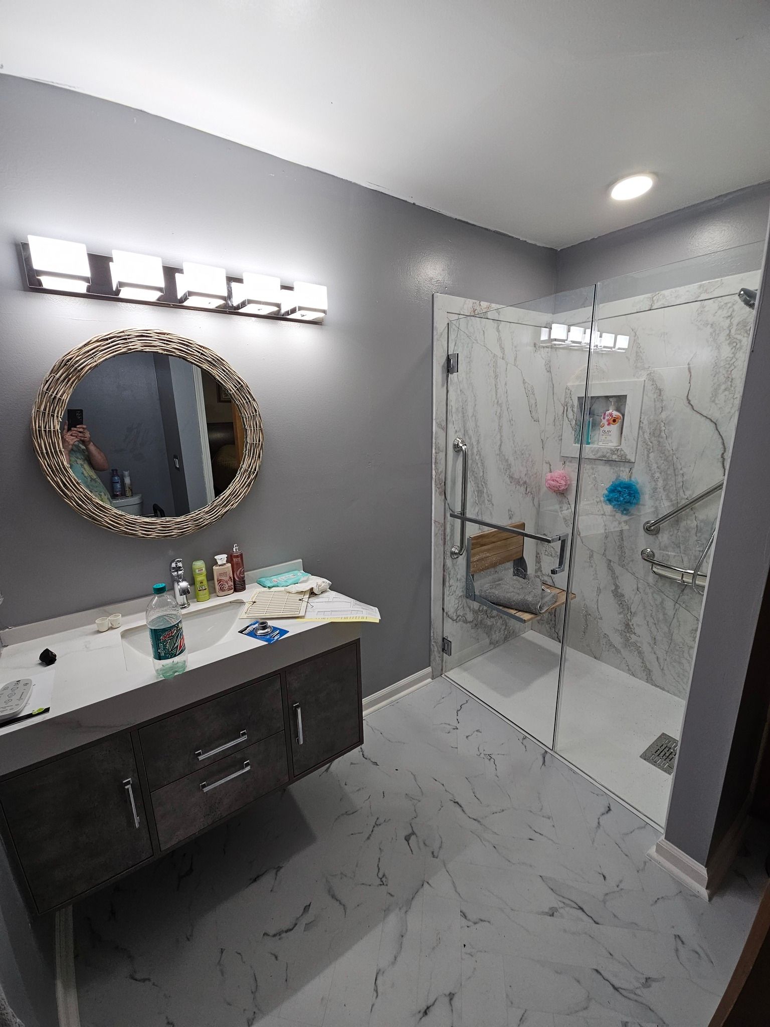 Modern bathroom with gray walls, marble-look shower, dark wood vanity, and round mirror.