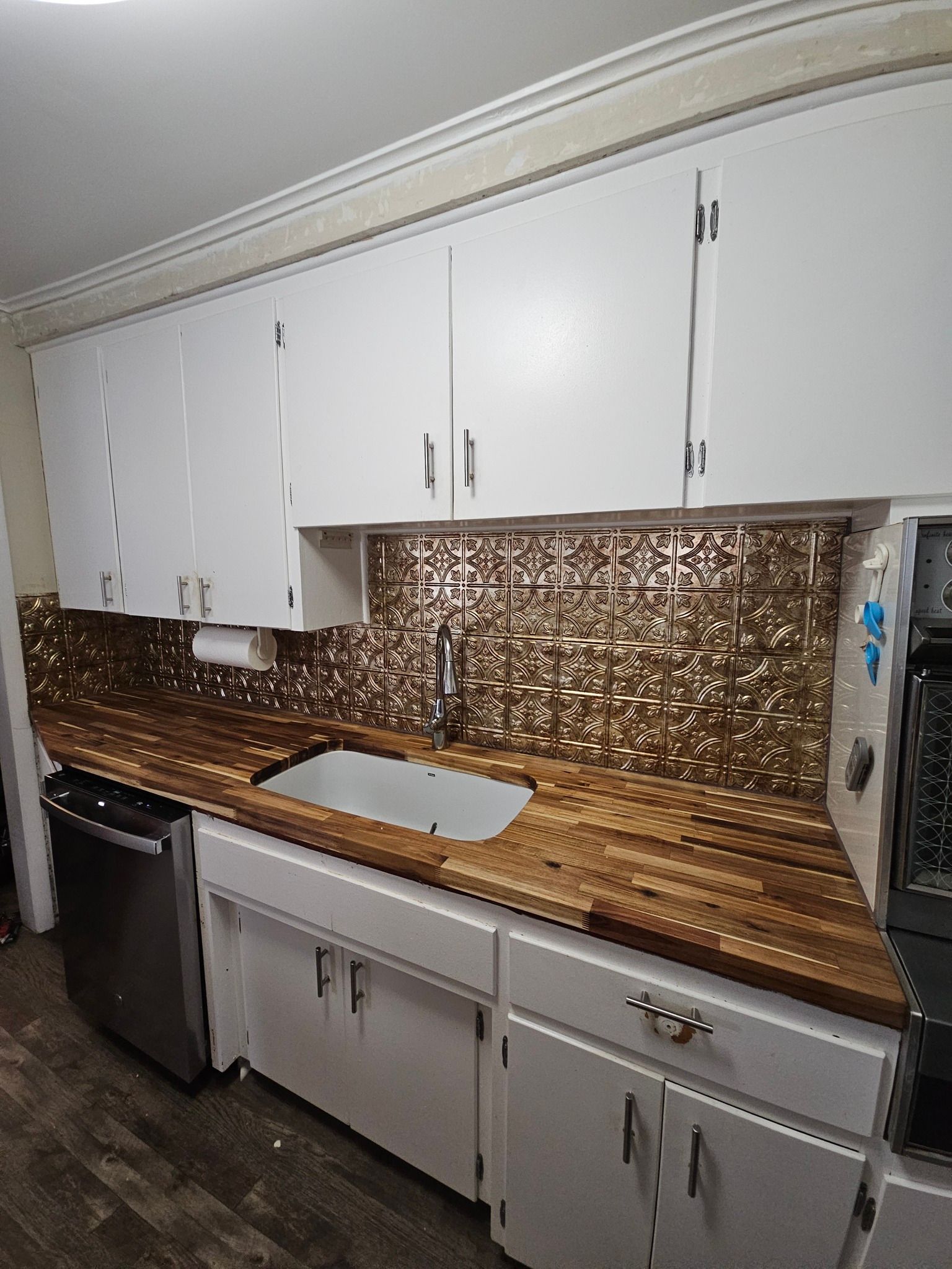 Kitchen with white cabinets, wood countertops, bronze backsplash, and stainless steel appliances.