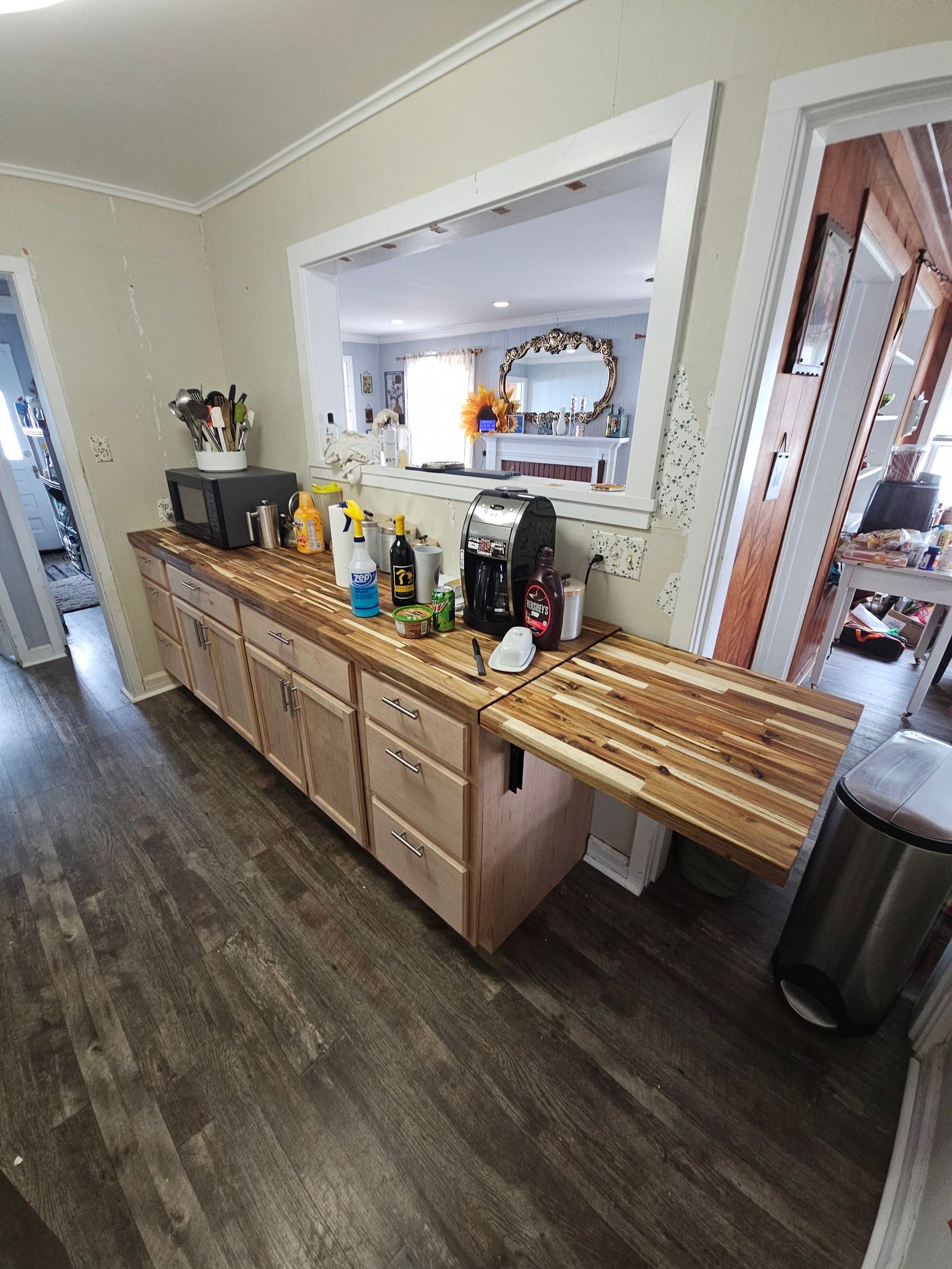 Wooden cabinet with countertop and appliances, a drop-down surface and open window to a living room.