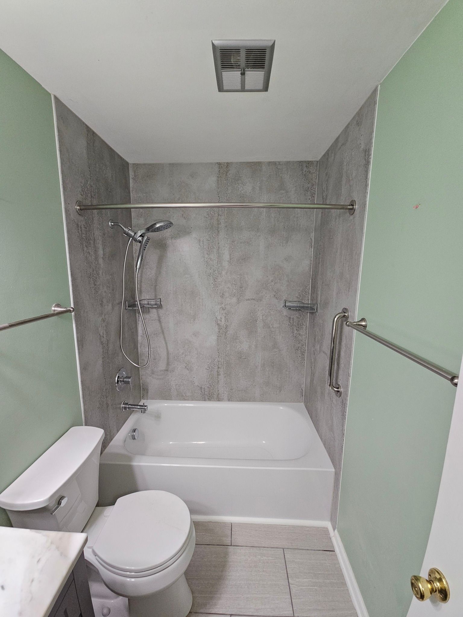 Bathroom with white tub, toilet, gray shower surround, and light green walls.