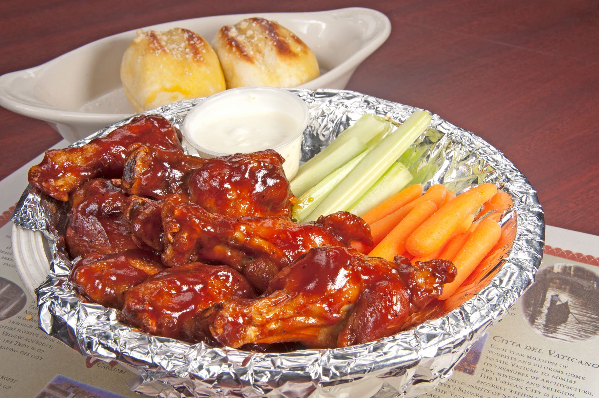 Chicken wings with sauce, vegetables, dipping sauce, and rolls.