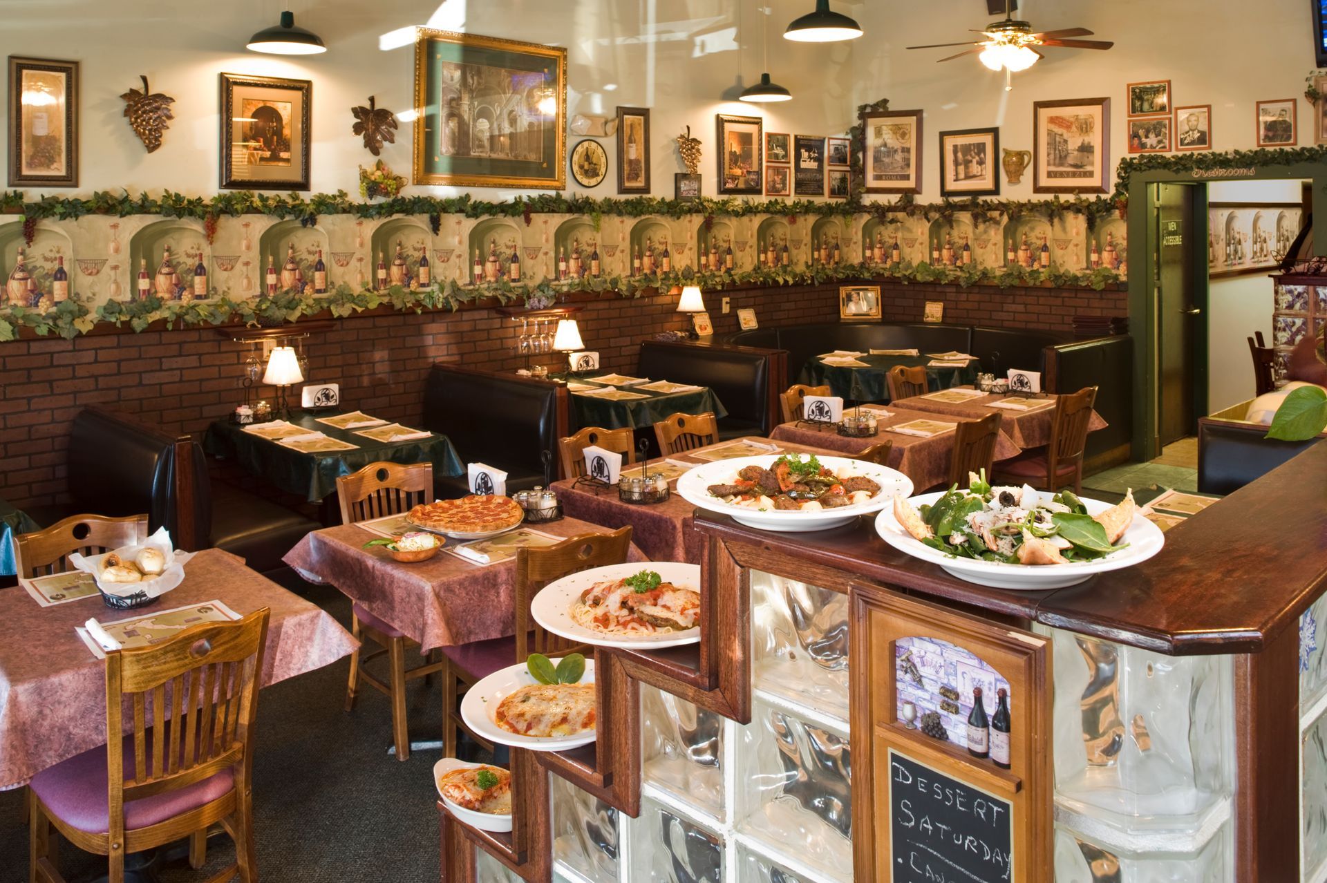Restaurant interior with tables, booths, decorative wallpaper, and food on a counter.