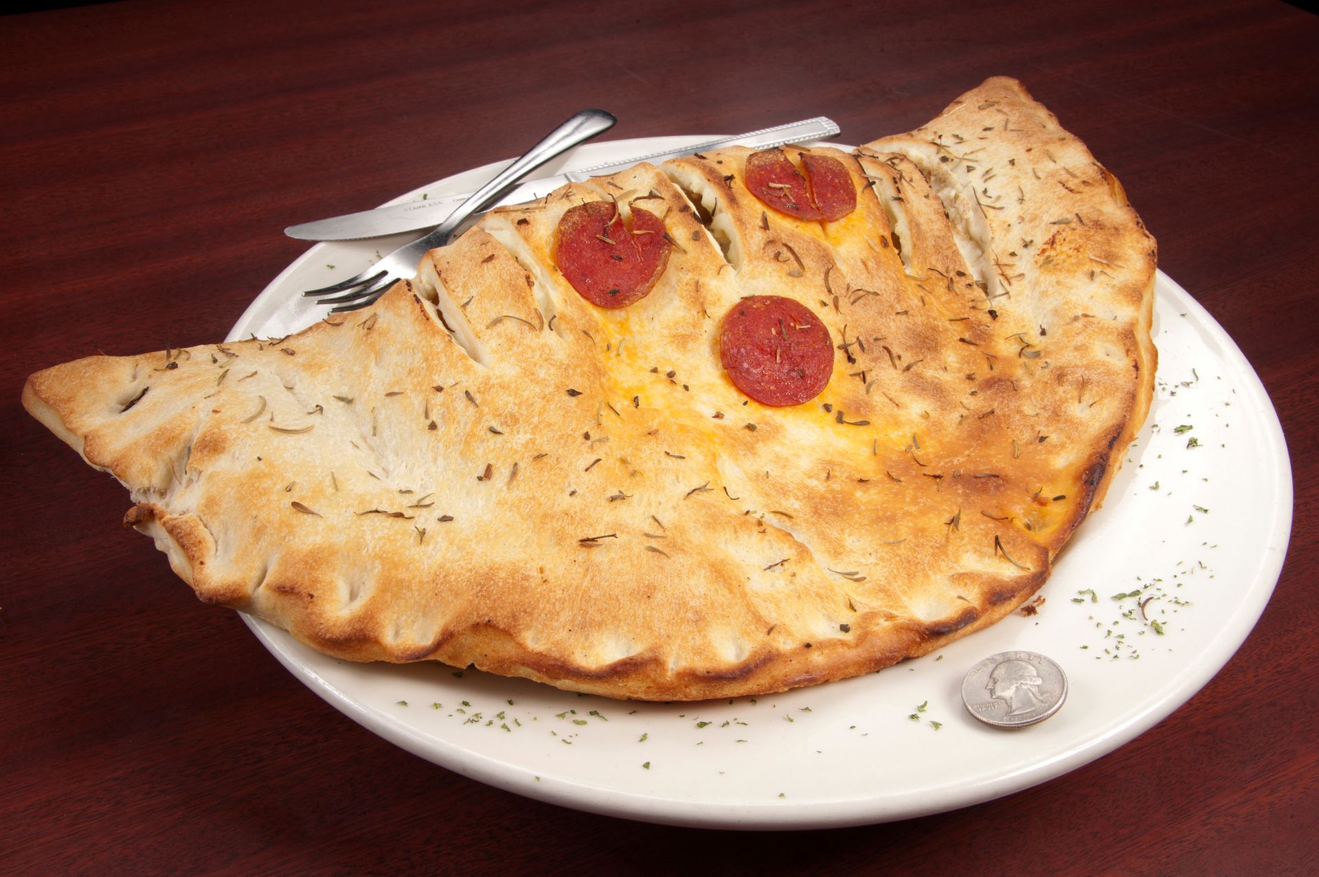 Calzone on a white plate with a knife and fork, topped with pepperoni.