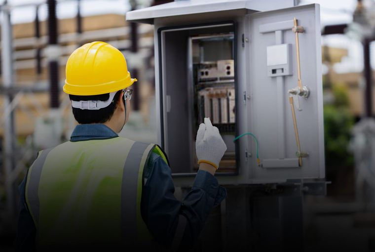 Worker in yellow hard hat inspecting an open electrical control box outdoors