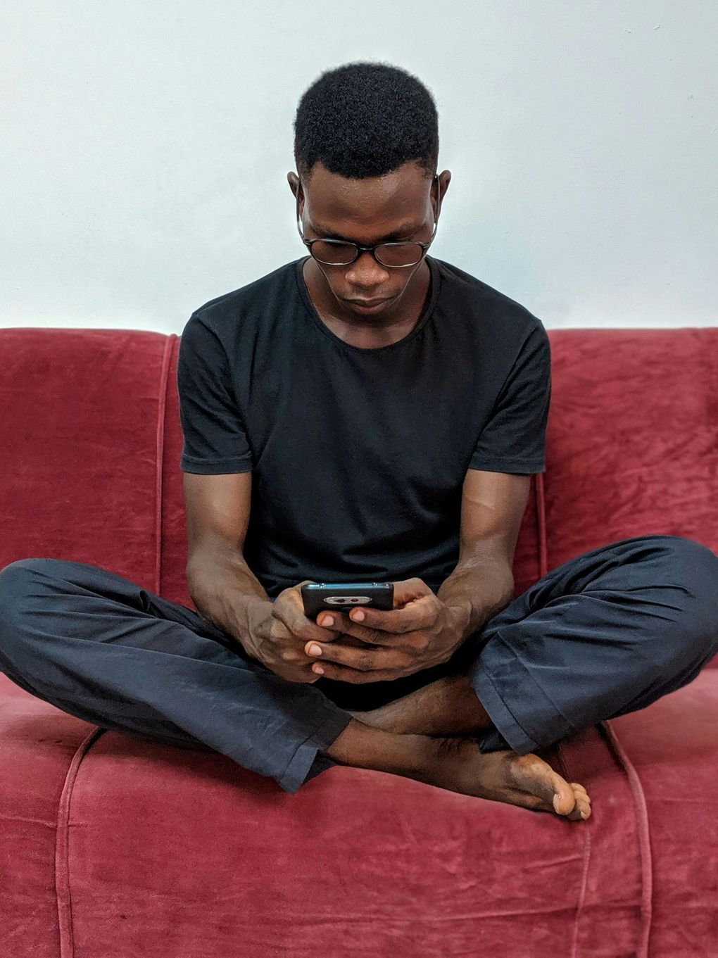 A man is sitting on a red couch looking at his cell phone.