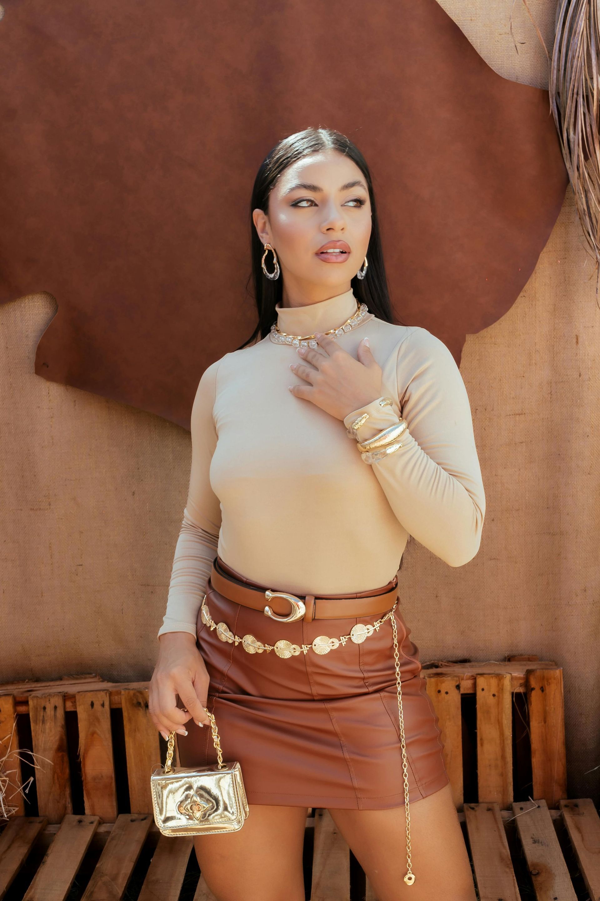 A woman wearing a turtleneck and a brown leather skirt is holding a purse.