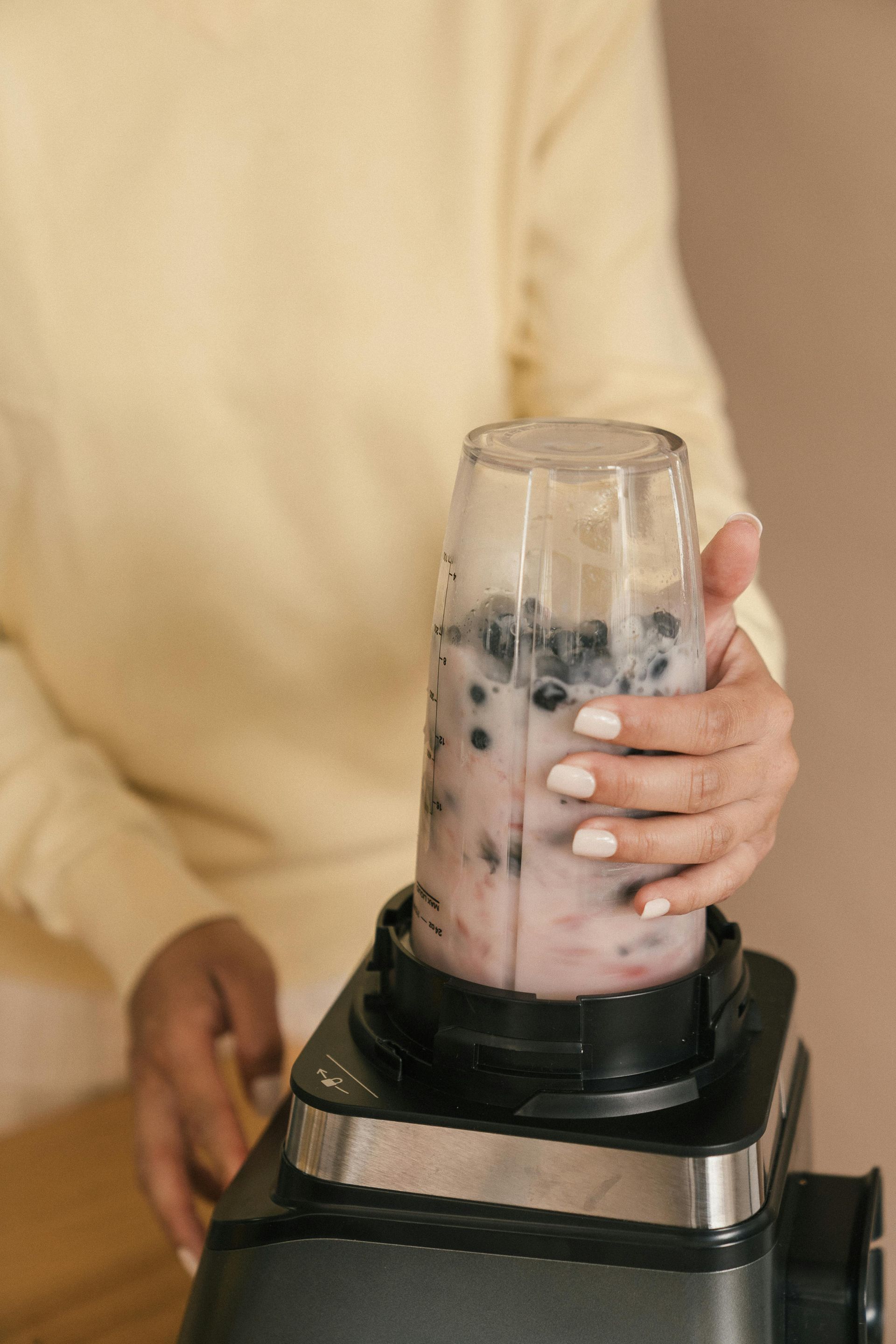 A woman is making a smoothie with blueberries in a blender.