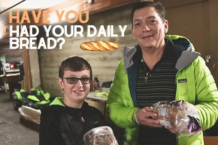 A man and a boy holding bread in front of a sign that says have you had your daily bread