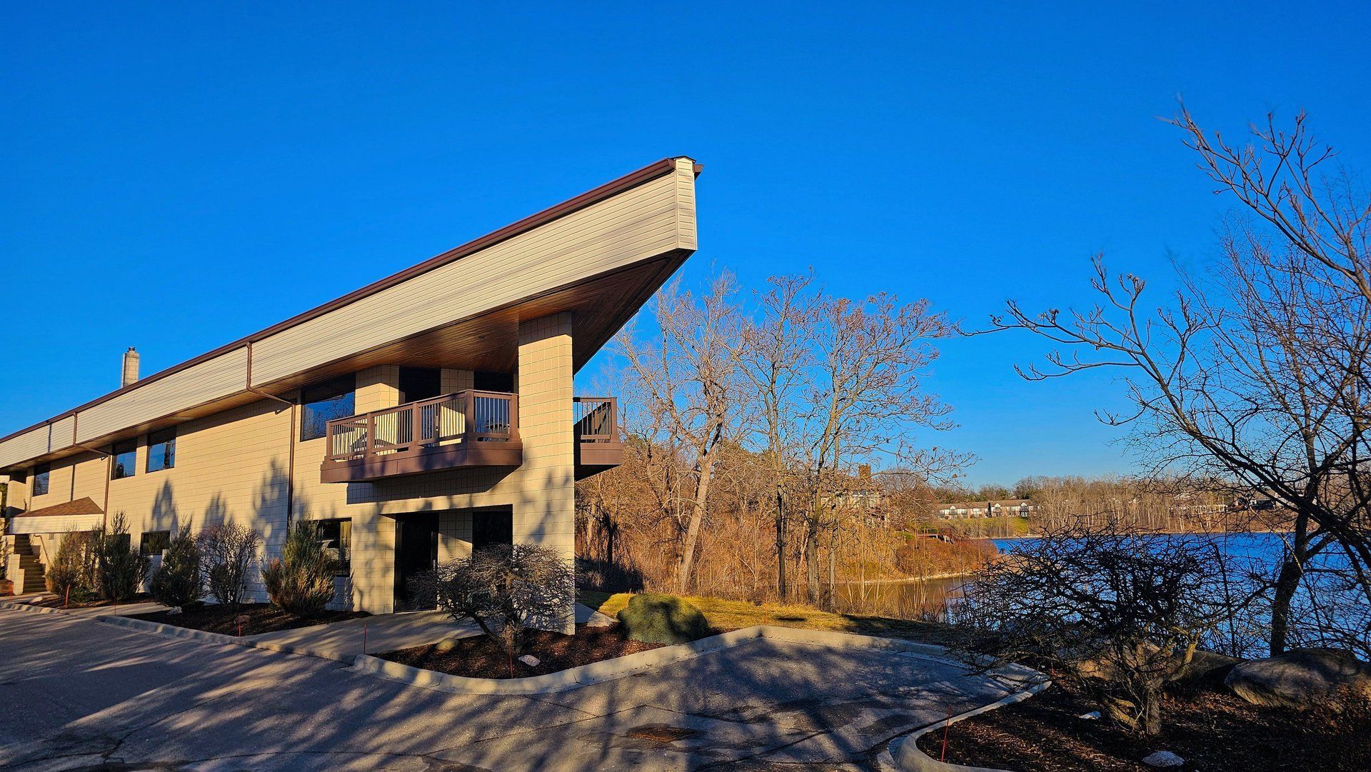 Two-story building with angled roof and balcony overlooking a body of water under a blue sky.