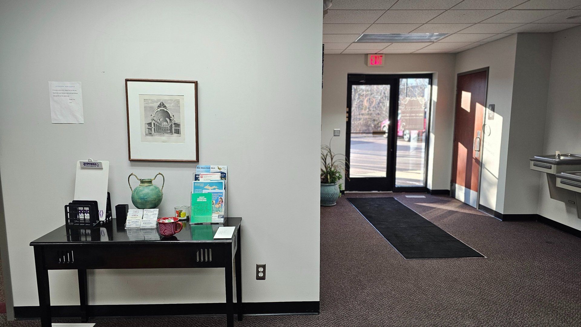 Hallway with a black table, framed art, and entrance doors with sunlight.