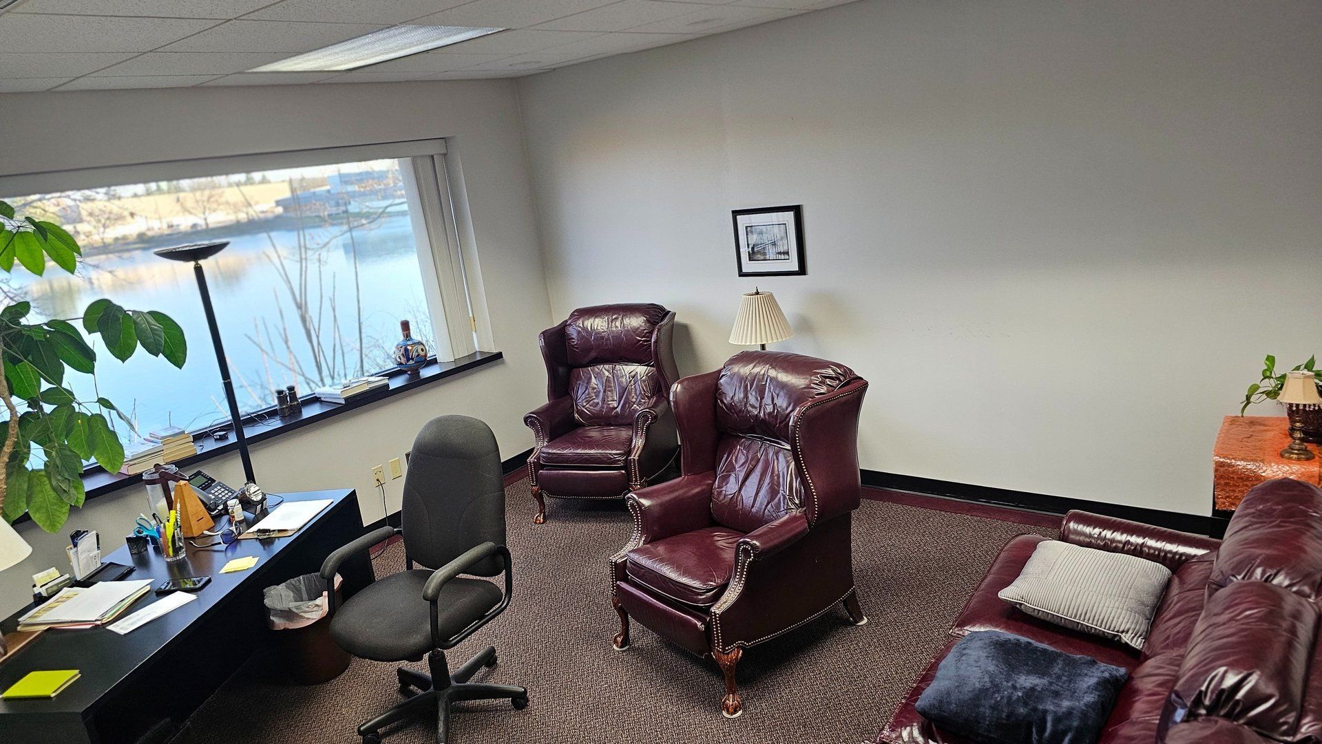 Office with two red armchairs, a couch, desk, and a window overlooking water.