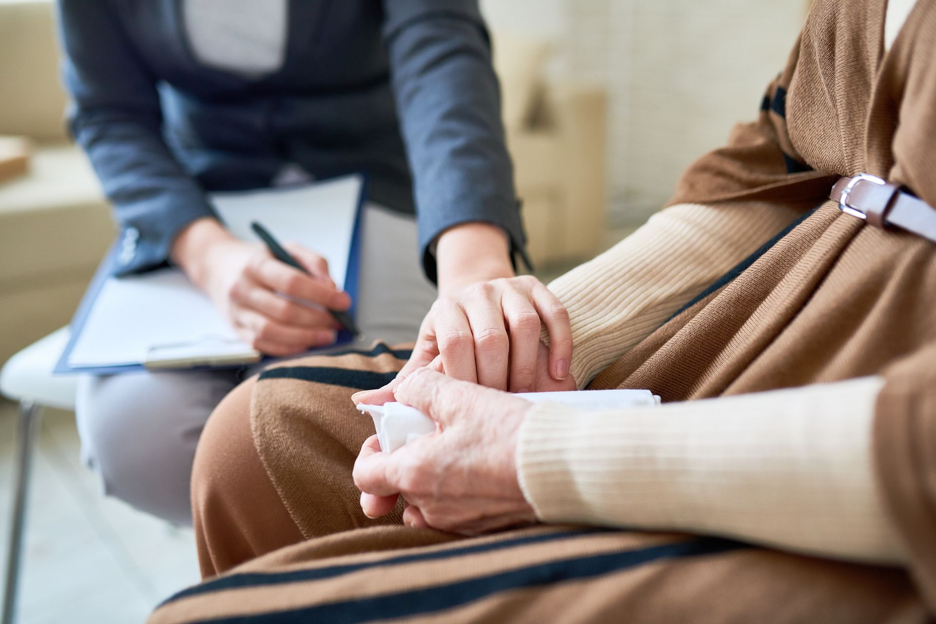 A person holding hands with another; the first person is writing notes on a clipboard.