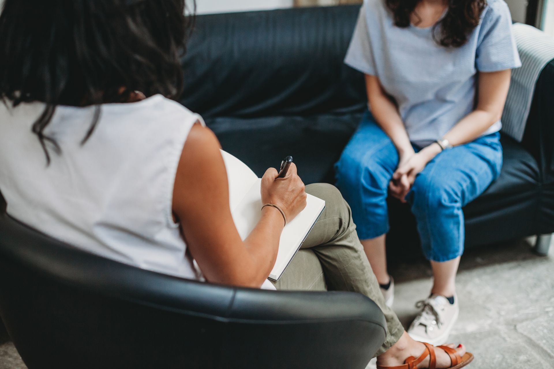 Therapist taking notes during a session with a patient seated on a black couch.