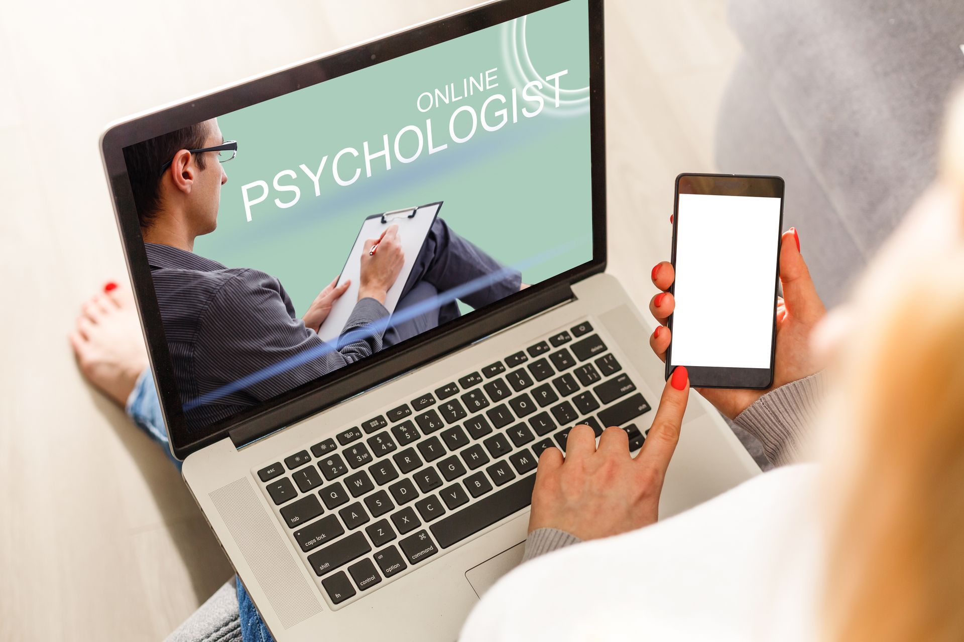 Person using laptop and smartphone for online therapy session.