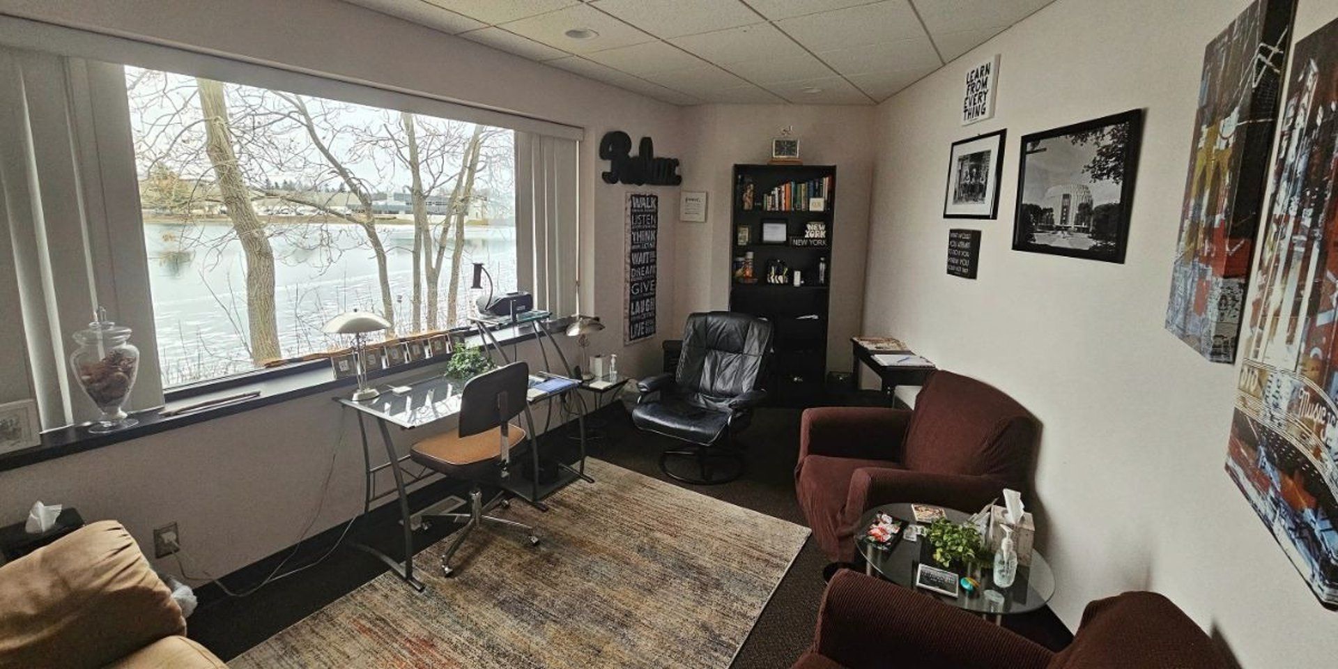 Cozy office with a lake view, desk, armchairs, and art.