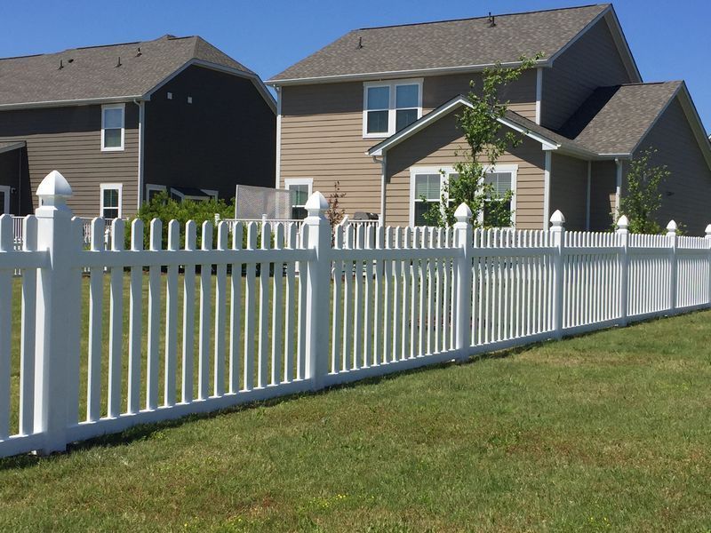 A white picket fence surrounds a lush green yard in front of a house.