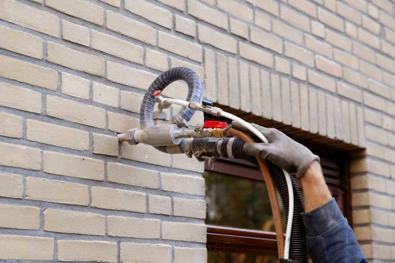 A man is spraying insulation on a brick wall.