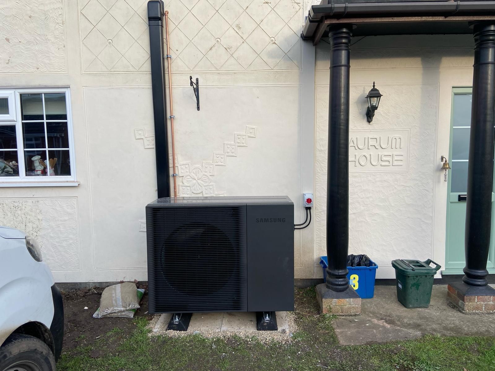 A black air conditioner is sitting outside of a white house.