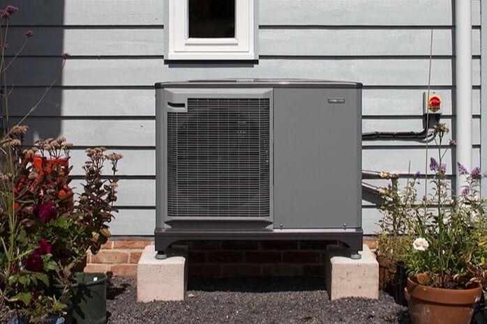 A gray air conditioner is on the side of a house.