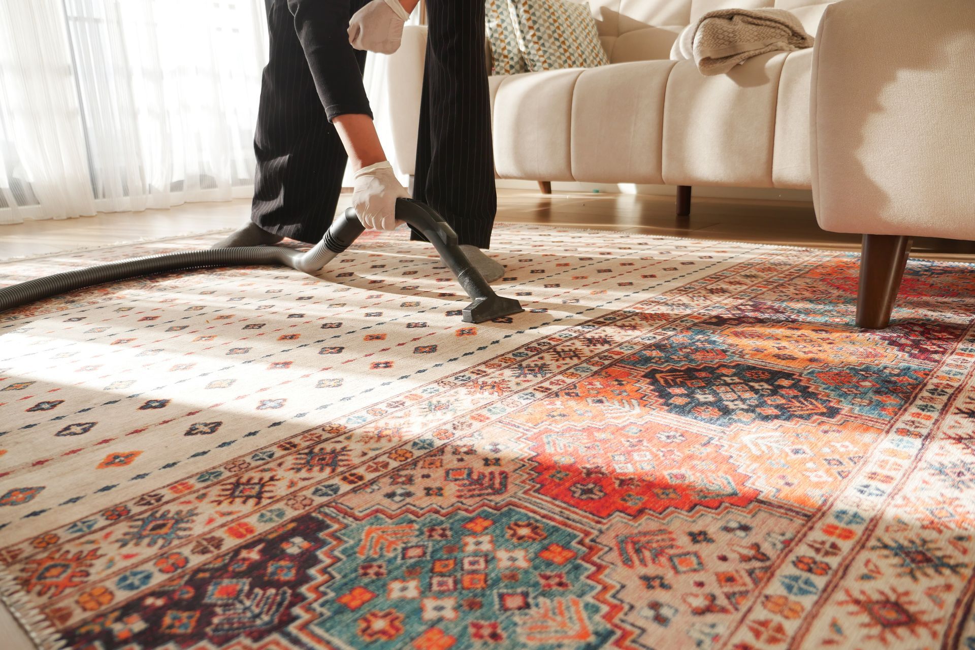 Person vacuuming a patterned rug in a living room near a sofa.