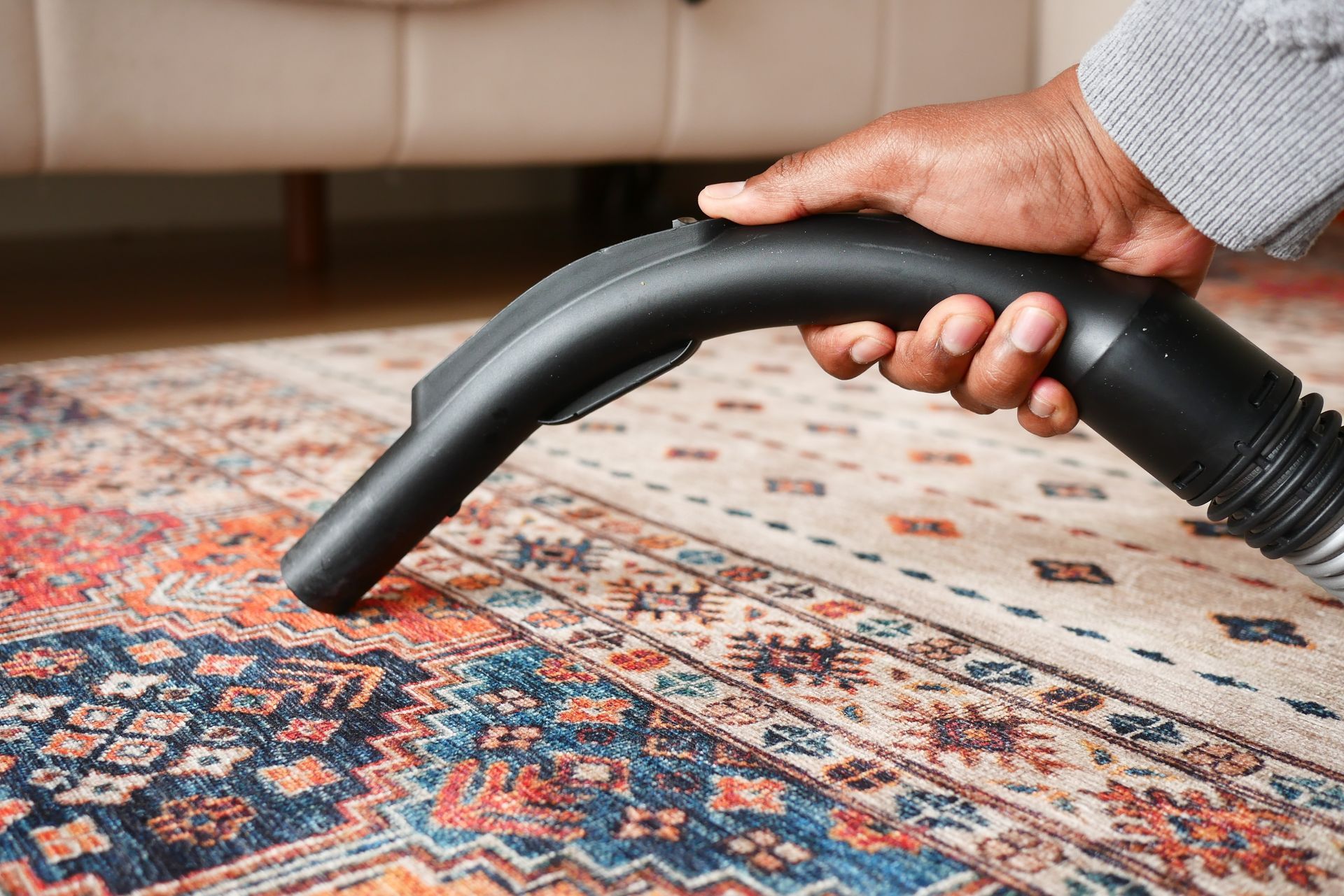 Person vacuuming a colorful rug in a living room.