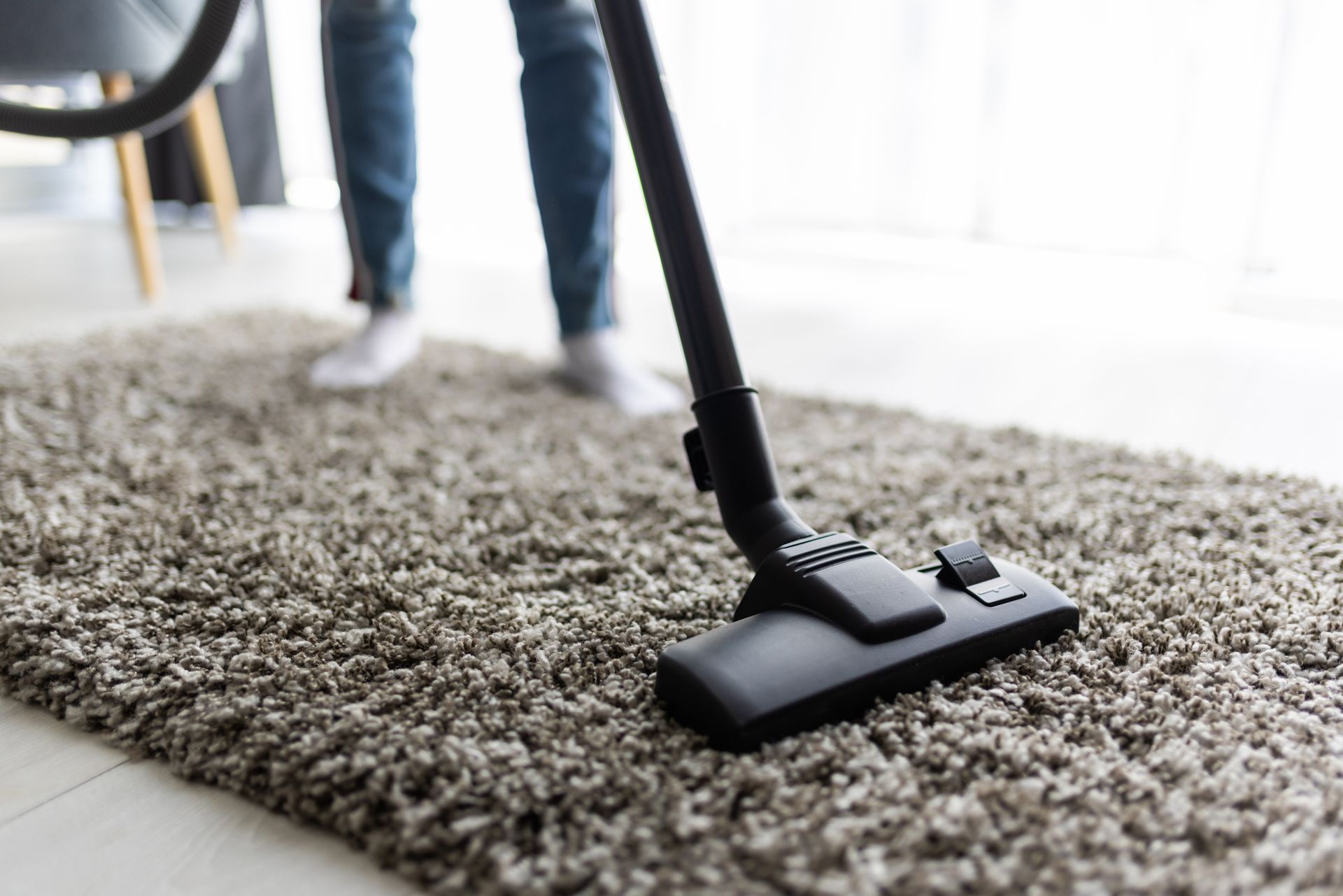 Vacuum cleaner head cleaning a gray shag rug in a bright room