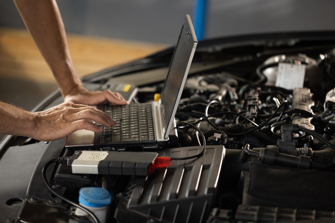 A Man is Working on a Laptop Computer Under the Hood of a Car — CJ's Holden Spares & Repairs in Queanbeyan West, NSW